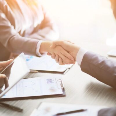 Shared handshake between coworkers over contract-laden table