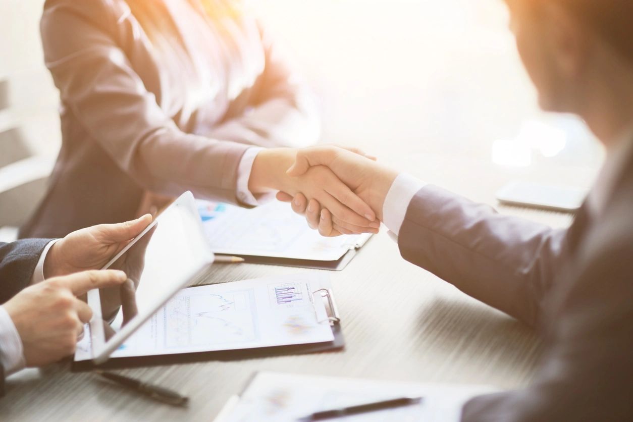 Shared handshake between coworkers over contract-laden table